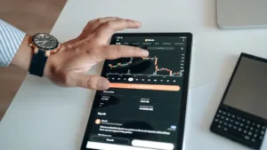 Mâna unui investitor indicând un grafic bursier în scădere pe o tabletă, ilustrând volatilitatea pieței